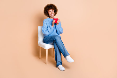 Full size photo of satisfied girl sitting on chair hold cup of coffee look at discount empty space isolated on pastel color backgroundの写真素材