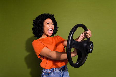 Portrait of nice young woman beep horn wheel wear orange t-shirt isolated on khaki color backgroundの写真素材