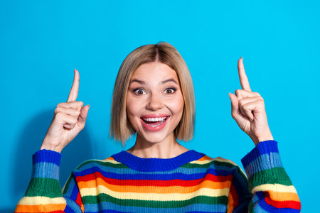 Photo of nice young woman direct fingers up empty space wear striped sweater isolated on blue color backgroundの写真素材