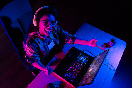 High angle view photo of young woman raise fists triumph play gaming laptop esport neon light night...
