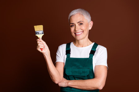 Photo of adorable lovely senior pretty woman wear uniform hold tool repair process isolated on brown color backgroundの写真素材