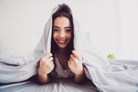 Photo of young sweet adorable lady lying bed covered blanket dressed sleepwear chill apartment waking up hotel bedroom white light interiorの写真素材