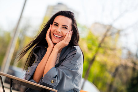 Photo of shiny attractive lady dressed grey coat arms cheeks sitting cafe enjoying good weather outdoors town streetの写真素材