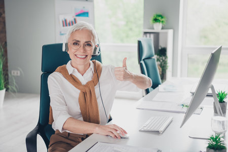 Photo of smart elderly chief female call center support thumb up wear formalwear comfortable modern office room interior indoors workspaceの写真素材