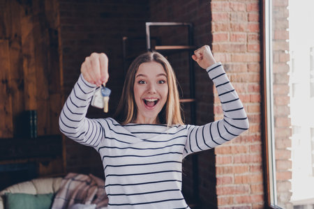 Photo of attractive teen female winning hold key real estate dressed striped outfit cozy day light home interior living roomの写真素材
