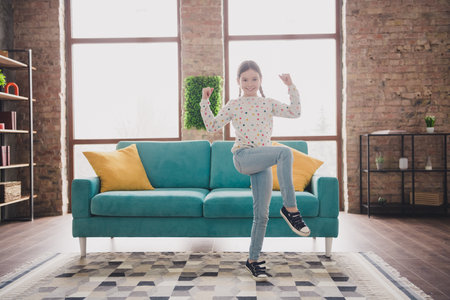 Full size photo of cute small schoolgirl raise fists wear pullover modern interior apartment indoorsの写真素材