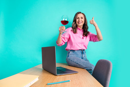 Photo of attractive senior woman working office drink wine thumb up dressed stylish pink clothes isolated on cyan color backgroundの写真素材