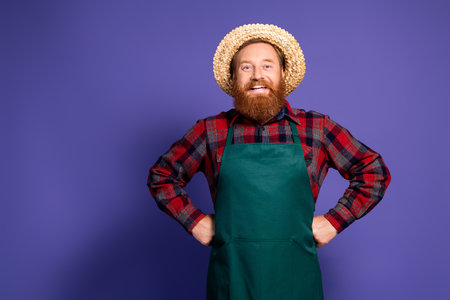 Photo of handsome mature man gardener hand waist wear green apron work filed isolated on purple color backgroundの写真素材