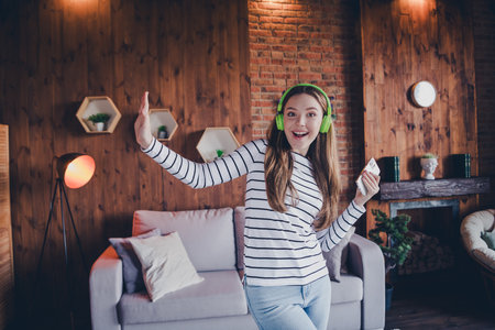 Photo of cute young girl dance phone headphones wear pullover modern loft interior apartment indoorsの写真素材