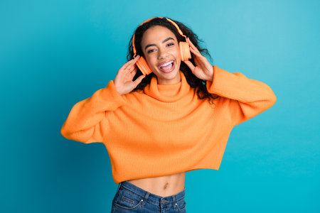 Photo of charming positive girl wear orange sweater headphones singing empty space isolated blue color backgroundの写真素材