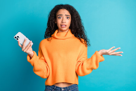 Photo of doubtful unsure girl wear orange sweater shrugging shoulders texting device empty space...