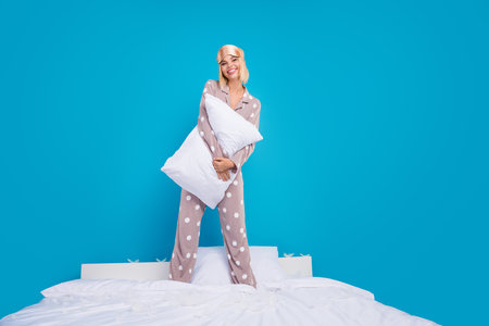 Full size photo of nice young woman stand bed hold pillow wear dotted pajama isolated on blue color backgroundの写真素材