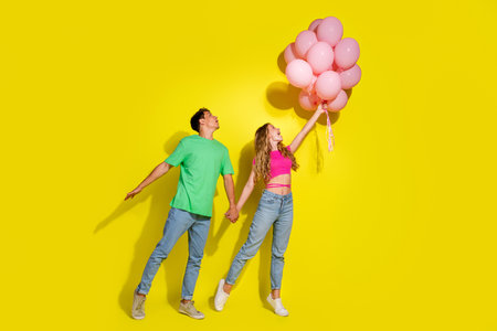 Full size photo of two nice young people hold arms balloons isolated on bright yellow color backgroundの写真素材