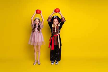 Full size photo of two kids halloween princess pirate costume hold pumpkin empty space isolated on yellow color backgroundの写真素材