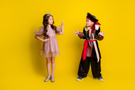 Full body portrait of two small kids point finger shrug shoulders halloween pirate princess costume isolated on yellow color backgroundの写真素材