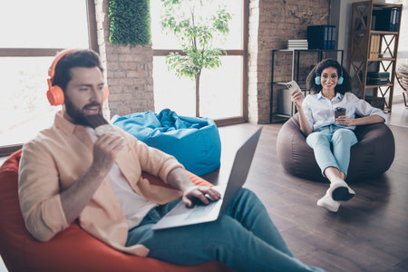 Portrait of two young corporate workers eat chocolate use laptop phone modern loft interior office indoorsの写真素材