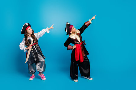 Full body portrait of two little kids direct fingers empty space halloween pirate costume isolated on blue color backgroundの写真素材
