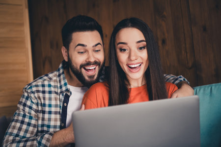 Photo of attractive trendy cheerful married young couple spending free time excited netbook eshop move new apartment home interior indoorsの写真素材