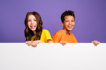 Photo of lovely two little kids white empty space banner dressed stylish orange yellow garment isolated on purple color backgroundの写真素材