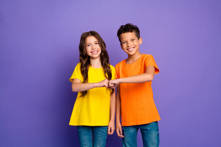 Photo portrait of cute little boy girl fist bump friends dressed stylish yellow orange clothes isolated on purple color backgroundの写真素材