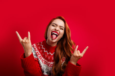 Photo of charming funky lady wearing ugly sweater ornament brutal rock roll lover showing horns sign isolated on red color backgroundの写真素材