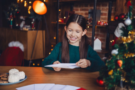 Photo of charming little girl write letter envelope dressed green christmas garment tradition atmosphere decor house indoors roomの写真素材
