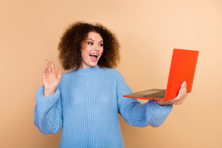 Photo of working specialist young business woman with laptop waving hand for colleagues greetings isolated on beige color backgroundの写真素材