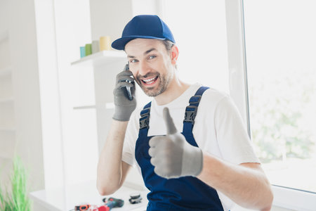 Confident handyman with thumbs up and phone, ready for home renovation and repair tasksの写真素材