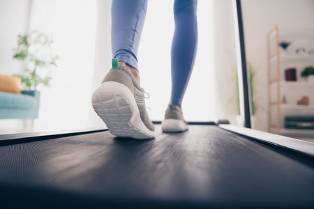 Woman in modern sportswear walking on treadmill in bright apartment with natural light and stylish decor, enjoying fitness and healthy lifestyle indoors.の写真素材