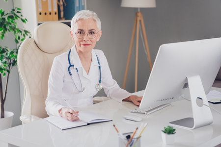 Photo of aged woman qualified doctor write notepad wear white coat workplace office indoorsの写真素材