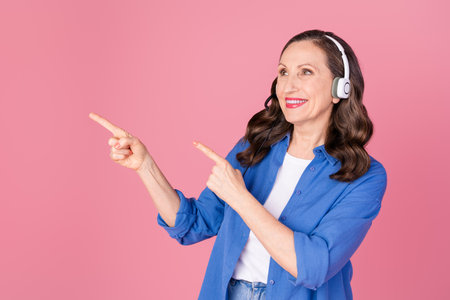 Photo portrait of nice pensioner female look point empty space call center wear trendy blue outfit isolated on pink color backgroundの写真素材