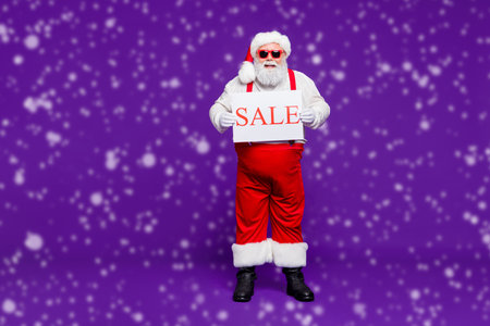 Full length body size view of his he nice confident cheerful cheery bearded thick fat Santa holding in hands demonstrating sale placard isolated on bright vivid shine vibrant violet lilac backgroundの写真素材