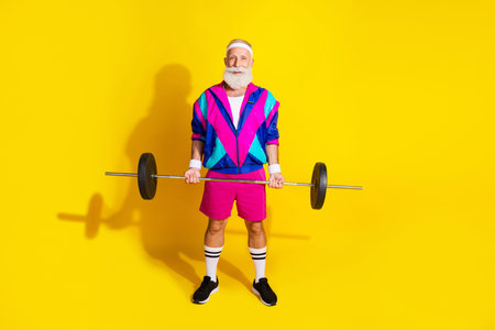 Full length photo banner of sportive cheerful old man lifting barbell dressed stylish retro sportswear isolated on yellow color backgroundの写真素材