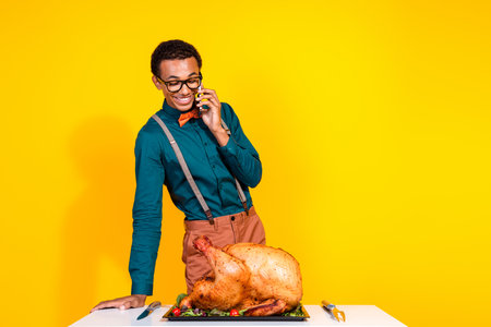 Photo of classy young man speak phone roasted thanksgiving turkey empty space isolated on yellow color backgroundの写真素材