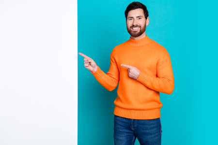 Photo of cheerful man wear trendy orange clothes introduce empty space isolated on cyan color backgroundの写真素材