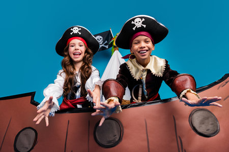 Photo of two small kids halloween pirate costume sail ship isolated on blue color backgroundの写真素材