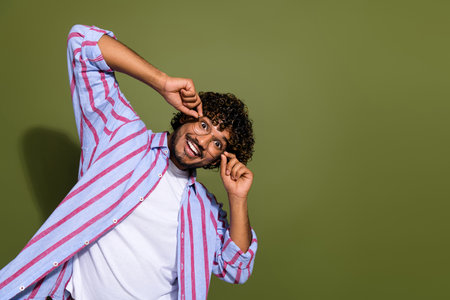 Portrait photo of handsome arab manager in striped casual shirt touching eyeglass advertising stylish accessory isolated on khaki color backgroundの写真素材