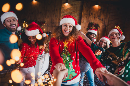 Photo of attractive young people pull hands follow have fun dancing new year decoration interior home party apartmentの写真素材