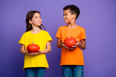 Photo of lovely two little kids hold pumpkins dressed stylish orange yellow garment isolated on purple color backgroundの写真素材