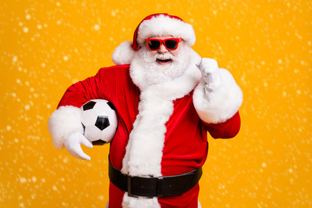 Portrait of his he nice attractive cheerful cheery Santa holding in hands ball celebrating having fun win winner luck attainment isolated over bright vivid shine vibrant yellow color backgroundの写真素材
