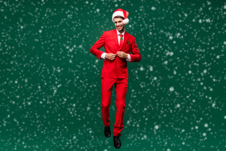Photo of cute sweet santa claus guy dressed red jacket headwear fixing button walking isolated green color backgroundの写真素材