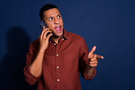 Photo of shocked impressed guy dressed brown shirt talking modern device showing emtpy space isolated blue color backgroundの写真素材