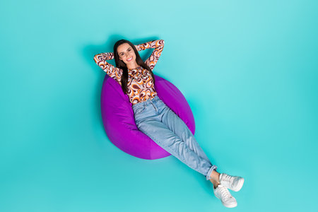 Full length top view photo of shiny attractive lady dressed retro shirt sitting bean bag arms behind head isolated blue color backgroundの写真素材