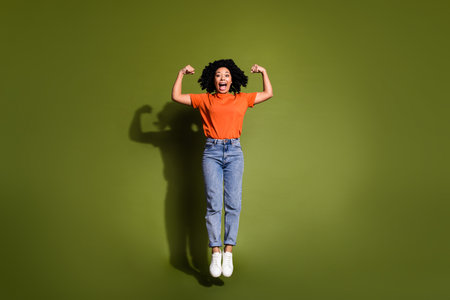 Full size photo of pretty young woman jump flex biceps wear t-shirt isolated on khaki color backgroundの写真素材