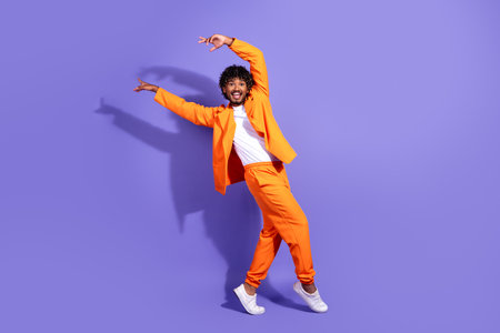 Full length photo of handsome good mood guy wear orange suit dancing smiling emtpy space isolated violet color backgroundの写真素材