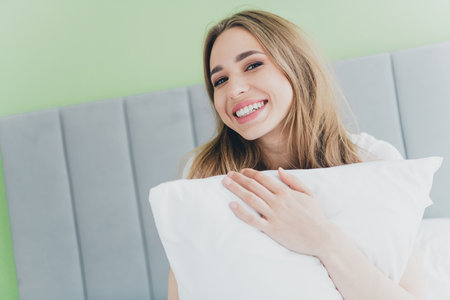 Photo of shiny cute girl nightwear smiling enjoying lying bed holding pillow indoors house apartment roomの写真素材