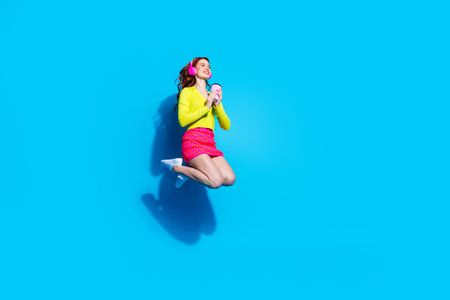 Full length photo of lovely young lady jump drink coffee headphones dressed stylish yellow garment...