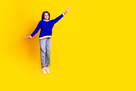 Full length photo of pretty teen girl jumping hanging wear trendy knitwear blue outfit isolated on yellow color backgroundの写真素材