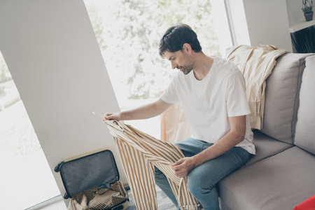 Young man relaxing at home, sorting clothes and enjoying leisure time on a sunny weekend in a cozy interiorの写真素材