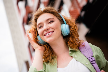 Joyful young redhaired woman enjoying music outdoors on a sunny day, radiating happiness and relaxationの写真素材